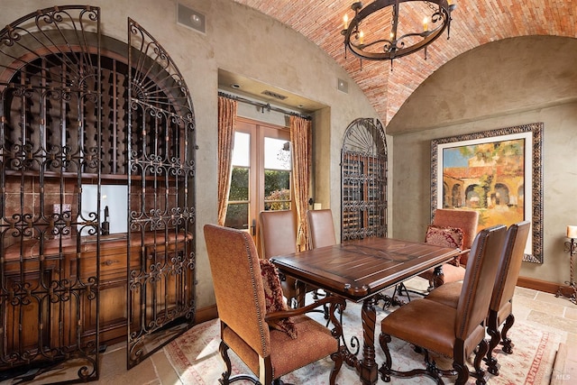 dining room featuring light tile flooring, vaulted ceiling, brick ceiling, and an inviting chandelier