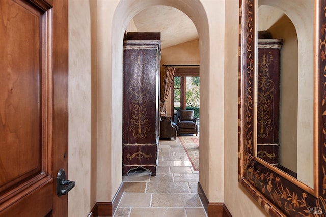 corridor with lofted ceiling and dark tile floors