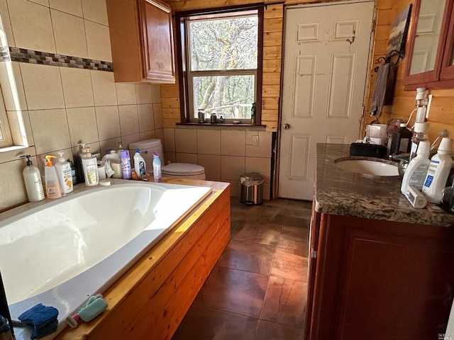 bathroom featuring a washtub, tile patterned flooring, toilet, vanity, and tile walls