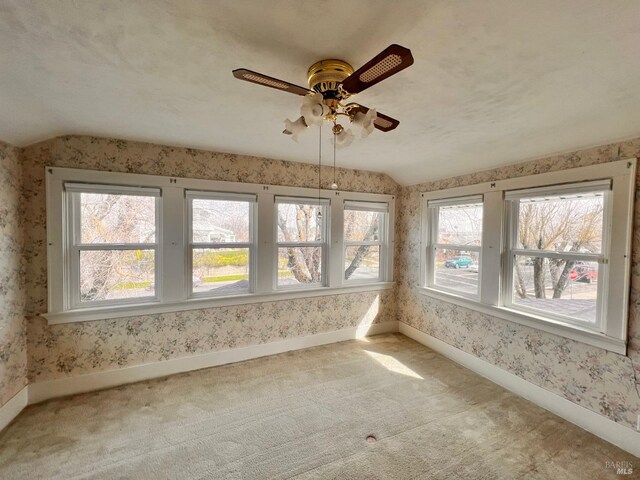 carpeted empty room featuring ceiling fan, vaulted ceiling, and a healthy amount of sunlight