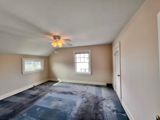 empty room with dark carpet, vaulted ceiling, ceiling fan, and a wealth of natural light