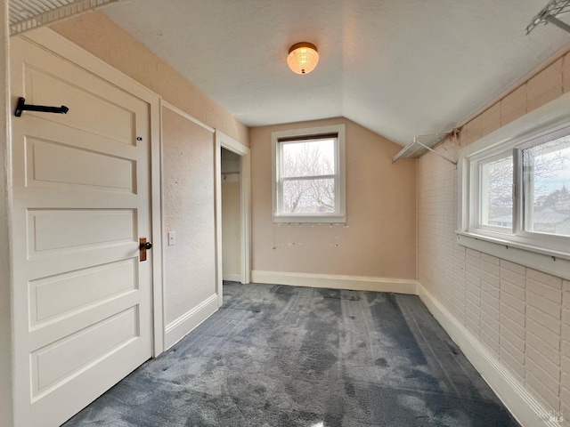 interior space featuring a textured ceiling, dark colored carpet, and vaulted ceiling