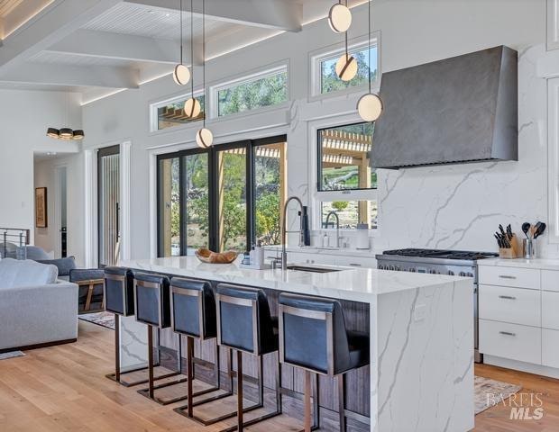 kitchen with white cabinetry, gas stove, a breakfast bar, wall chimney exhaust hood, and pendant lighting