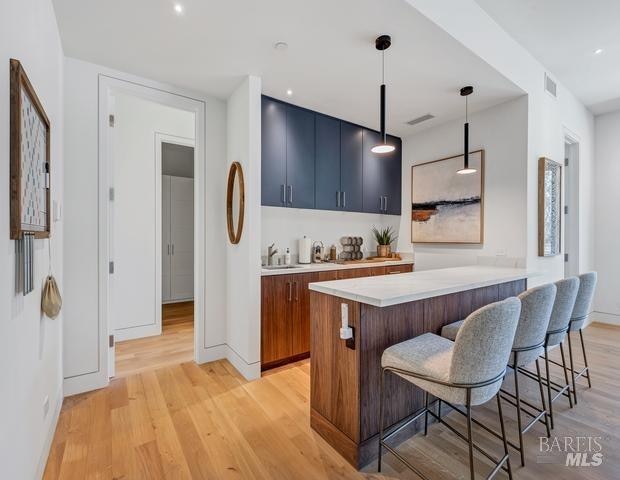 kitchen featuring decorative light fixtures, kitchen peninsula, light wood-type flooring, sink, and a kitchen breakfast bar