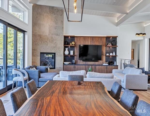 dining room with a tile fireplace, light wood-type flooring, beamed ceiling, and a high ceiling