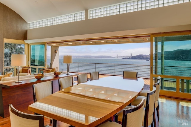 dining space with a water and mountain view, high vaulted ceiling, and wood-type flooring