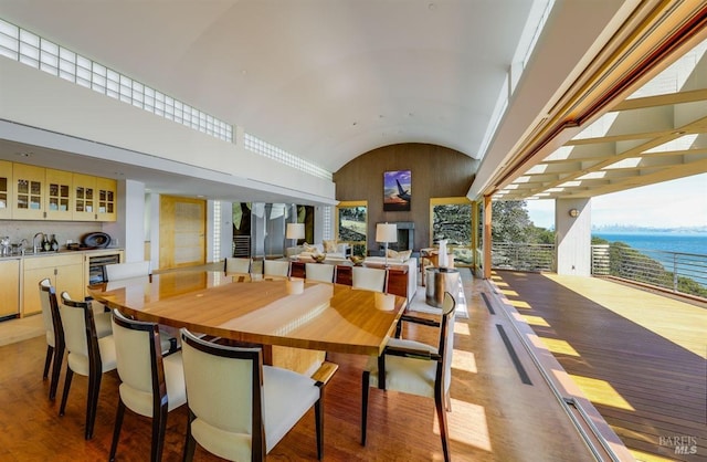 dining space with a water view, light hardwood / wood-style flooring, and vaulted ceiling