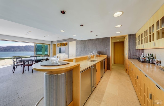 kitchen featuring sink, a water and mountain view, an island with sink, and light tile floors