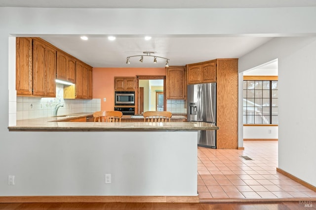 kitchen featuring light tile patterned flooring, kitchen peninsula, stainless steel appliances, and backsplash