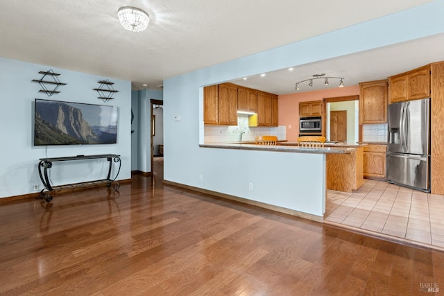 kitchen with kitchen peninsula, light hardwood / wood-style floors, stainless steel appliances, and tasteful backsplash