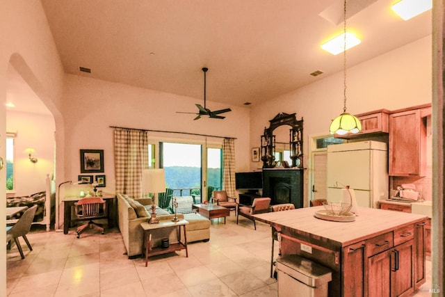 interior space featuring ceiling fan, white refrigerator, light tile flooring, high vaulted ceiling, and a center island
