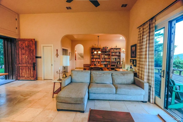 living room with ceiling fan with notable chandelier, light tile floors, and a towering ceiling