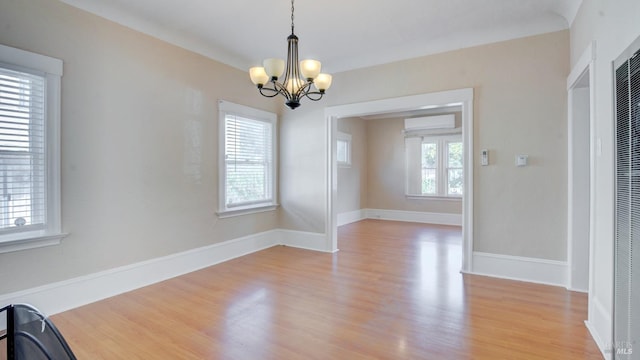 unfurnished room featuring plenty of natural light, an inviting chandelier, an AC wall unit, and light hardwood / wood-style flooring