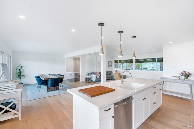 kitchen featuring decorative light fixtures, sink, light hardwood / wood-style flooring, a center island with sink, and dishwasher