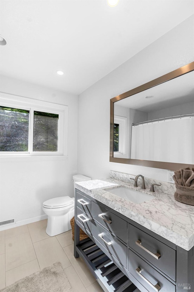 bathroom with toilet, tile flooring, vanity, and a wealth of natural light