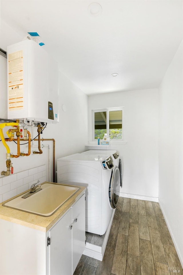 laundry area featuring water heater, washing machine and clothes dryer, sink, hardwood / wood-style floors, and cabinets