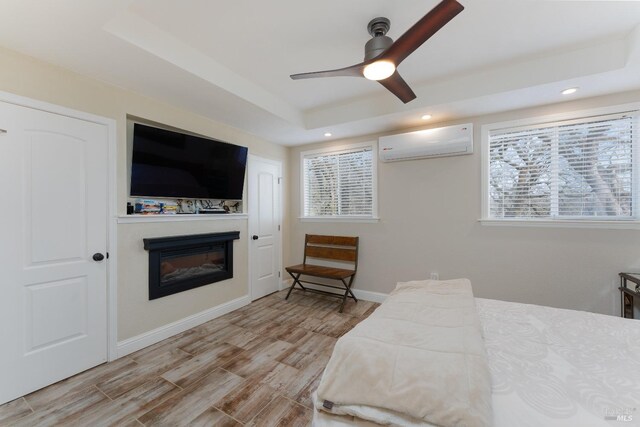 bedroom with ceiling fan, light hardwood / wood-style flooring, a raised ceiling, and a wall mounted AC