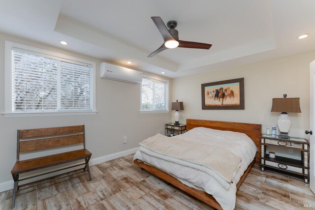 bedroom with a raised ceiling, light hardwood / wood-style floors, ceiling fan, and an AC wall unit