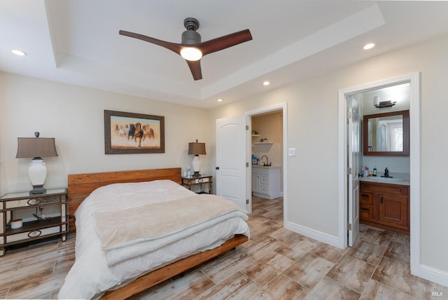 bedroom featuring ensuite bath, ceiling fan, and a tray ceiling