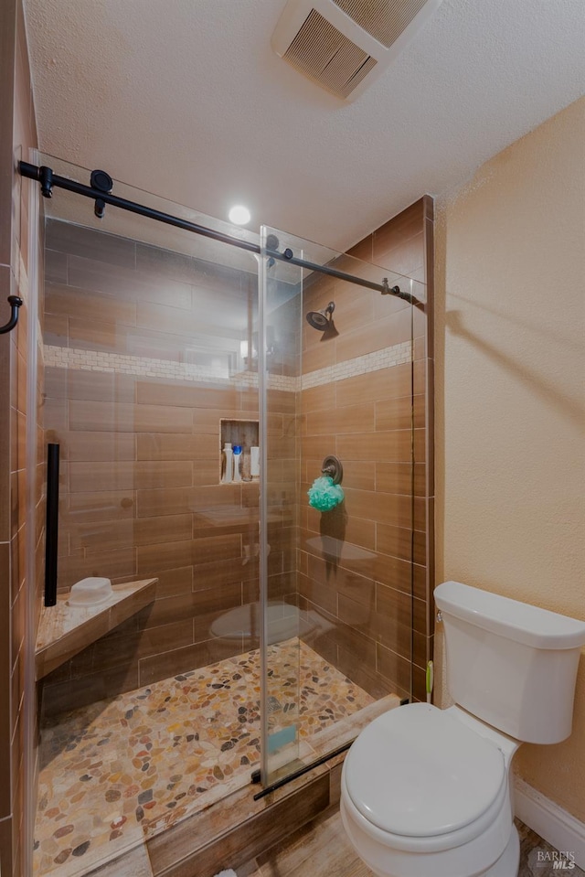 bathroom with walk in shower, toilet, and a textured ceiling