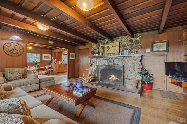 living room featuring wood walls, a stone fireplace, beam ceiling, and light hardwood / wood-style flooring