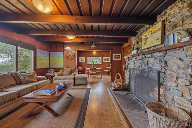 living room featuring a stone fireplace, hardwood / wood-style floors, beamed ceiling, and wooden ceiling