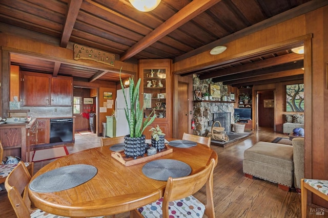 dining space featuring wooden ceiling, beamed ceiling, a stone fireplace, light hardwood / wood-style flooring, and wooden walls