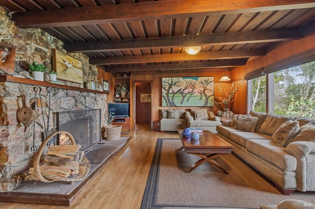 living room with a stone fireplace, wooden walls, hardwood / wood-style flooring, wooden ceiling, and beamed ceiling