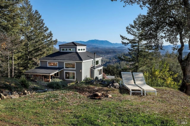 back of property with a mountain view and a lawn