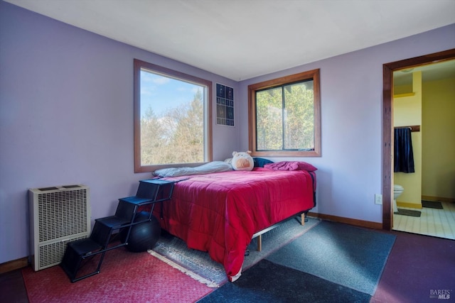 bedroom featuring heating unit, multiple windows, and ensuite bath