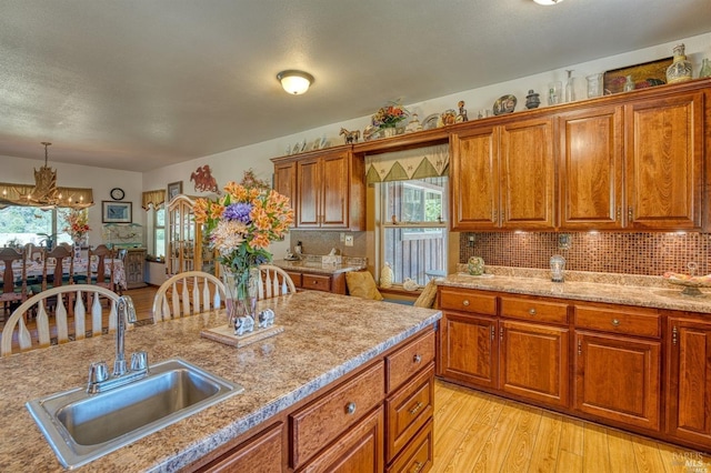 kitchen featuring pendant lighting, sink, a notable chandelier, light hardwood / wood-style floors, and decorative backsplash