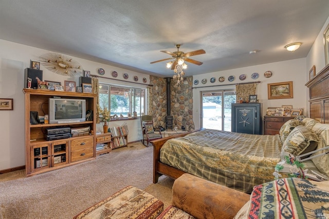 carpeted bedroom featuring a wood stove, ceiling fan, access to exterior, and a textured ceiling