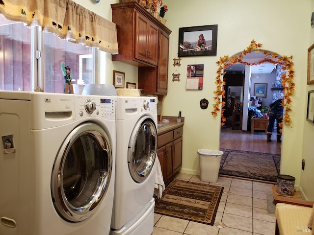 clothes washing area featuring light tile patterned floors, washer and dryer, and cabinets