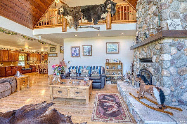 living room featuring ceiling fan, a stone fireplace, light hardwood / wood-style flooring, high vaulted ceiling, and wooden ceiling