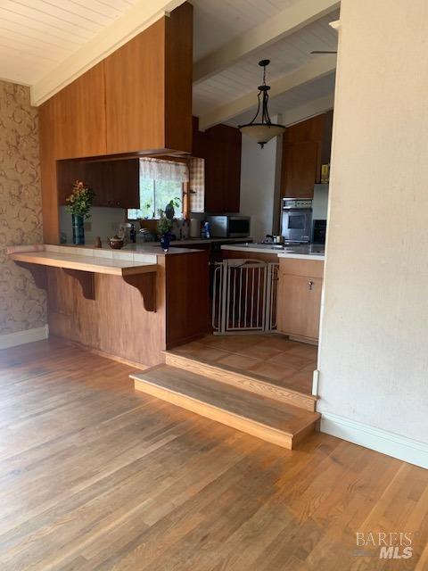 kitchen with a kitchen breakfast bar, oven, decorative light fixtures, light hardwood / wood-style floors, and kitchen peninsula