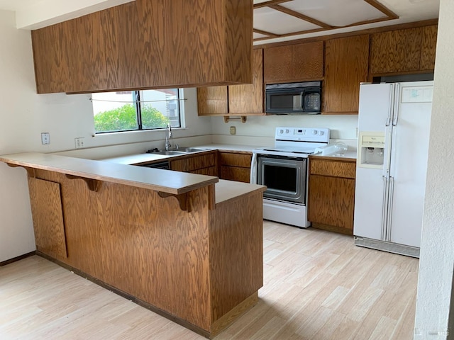 kitchen with a peninsula, white appliances, light wood-style floors, and a sink