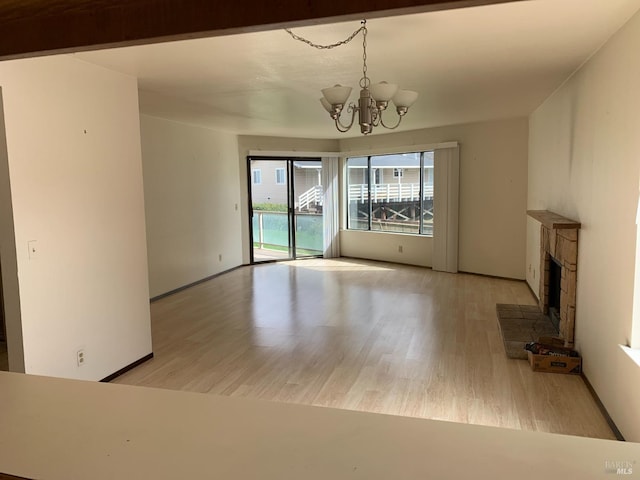 unfurnished living room with a notable chandelier, a fireplace, baseboards, and wood finished floors