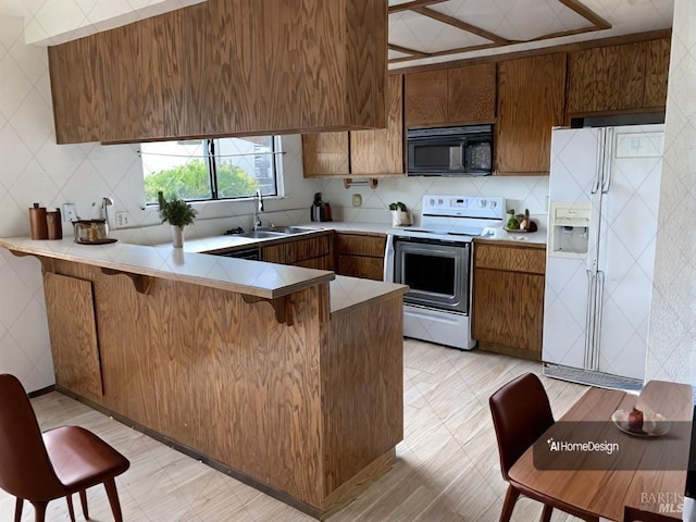 kitchen featuring light countertops, brown cabinetry, a sink, white appliances, and a peninsula