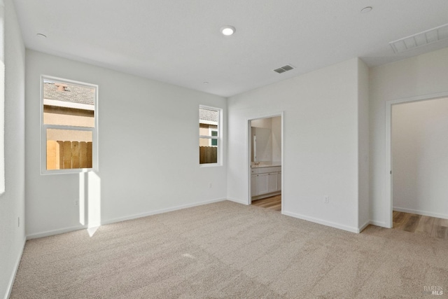 unfurnished bedroom with ensuite bath, light colored carpet, and multiple windows