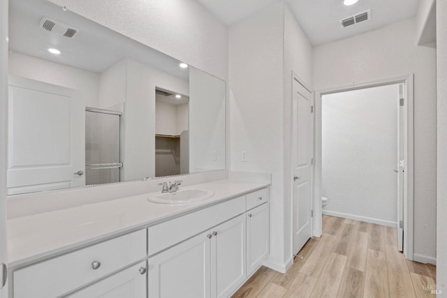 bathroom with hardwood / wood-style floors, vanity, a shower with shower door, and toilet