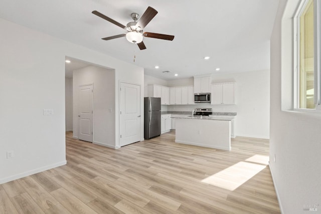 kitchen with white cabinets, light wood-type flooring, stainless steel appliances, and an island with sink