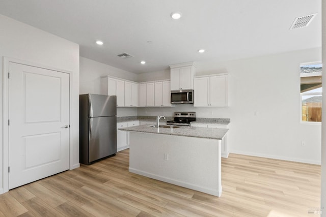 kitchen featuring light stone countertops, stainless steel appliances, a center island with sink, white cabinets, and light hardwood / wood-style floors