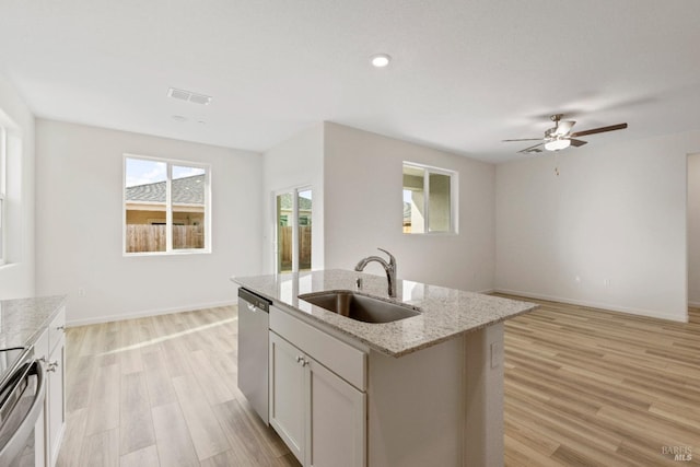 kitchen with light stone countertops, appliances with stainless steel finishes, sink, light hardwood / wood-style flooring, and an island with sink