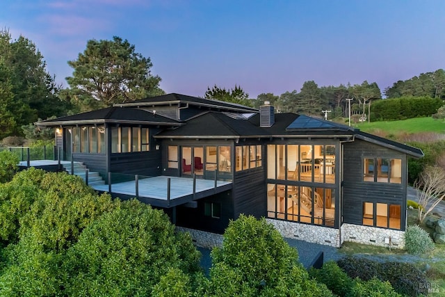 rear view of property with a deck, a sunroom, a chimney, and roof mounted solar panels