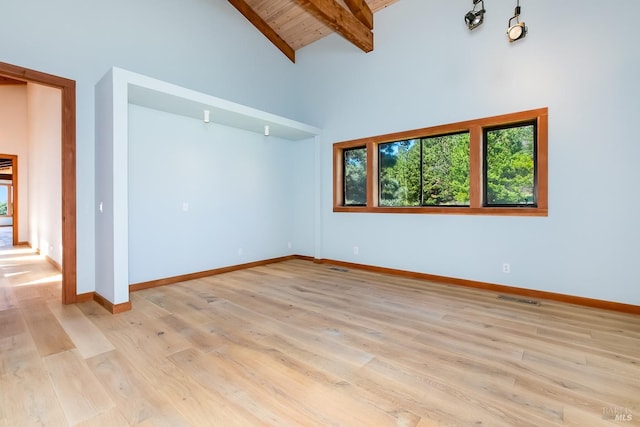 empty room featuring baseboards, light wood-style floors, visible vents, beam ceiling, and high vaulted ceiling