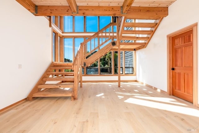 unfurnished living room featuring beam ceiling, stairway, and wood finished floors