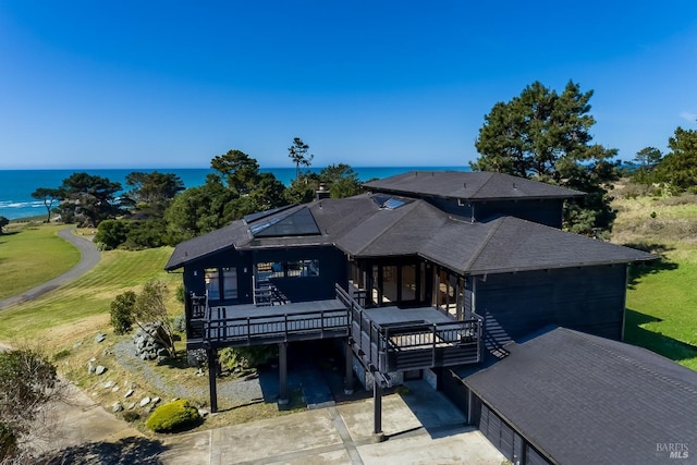 view of front facade with roof mounted solar panels, a chimney, a deck with water view, driveway, and roof with shingles