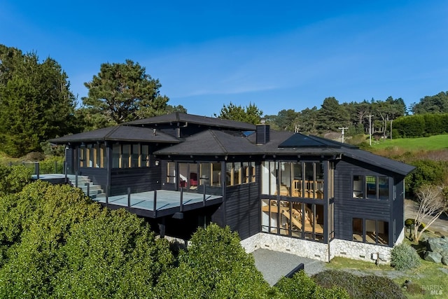 rear view of house featuring a deck, a sunroom, and a chimney