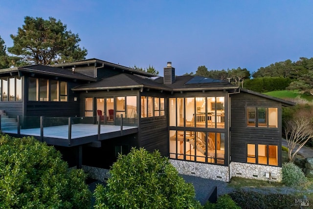 rear view of property featuring a deck, solar panels, a sunroom, and a chimney