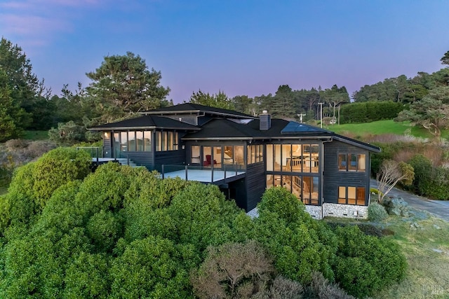 rear view of house with a wooden deck, a sunroom, and a chimney